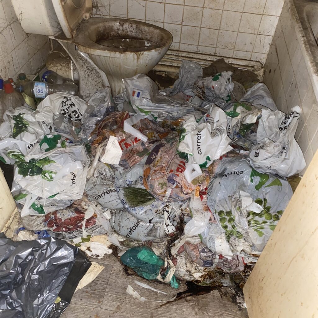 Salle de bain insalubre à Martigues, remplie de déchets plastiques, WC souillés et murs sales avant intervention de nettoyage extrême